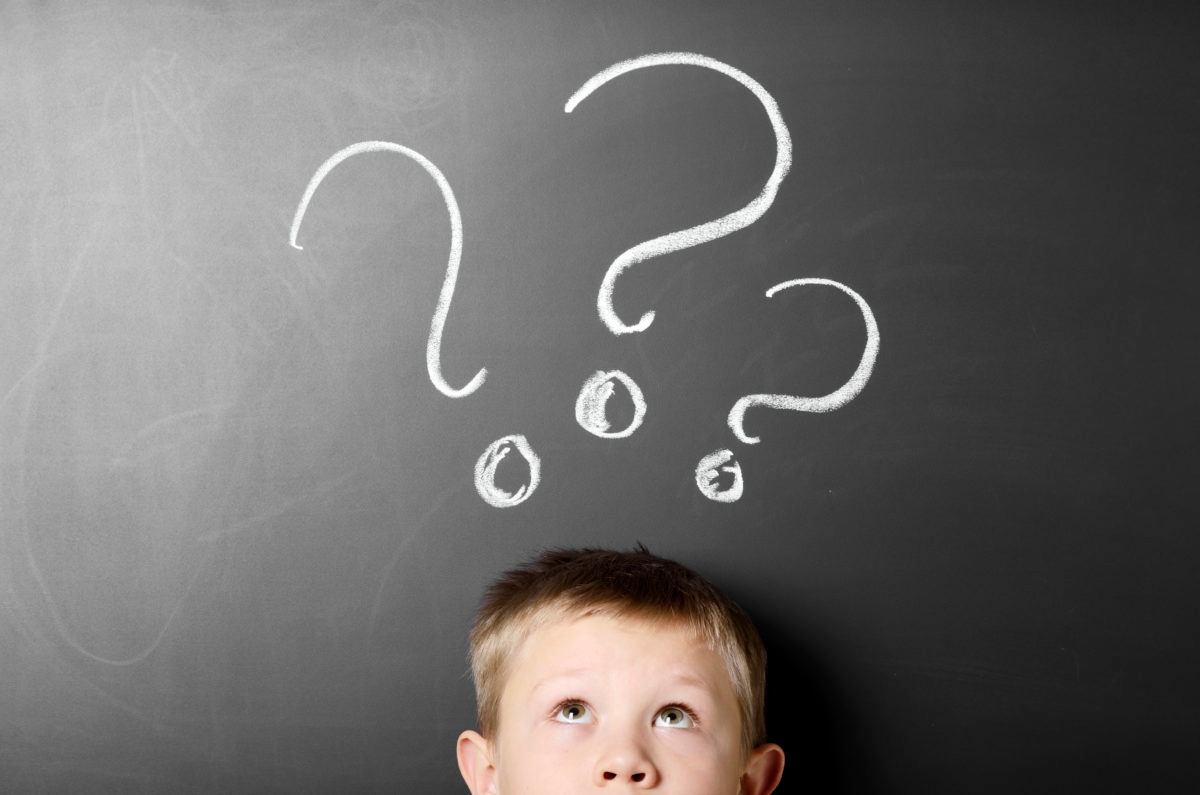 Wondering boy against chalkboard with a drawing of question marks.