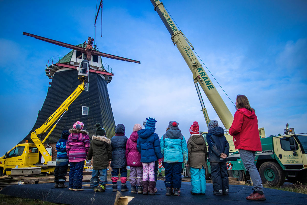 schoolchildren and teacher observe the lifting of a mill cap.