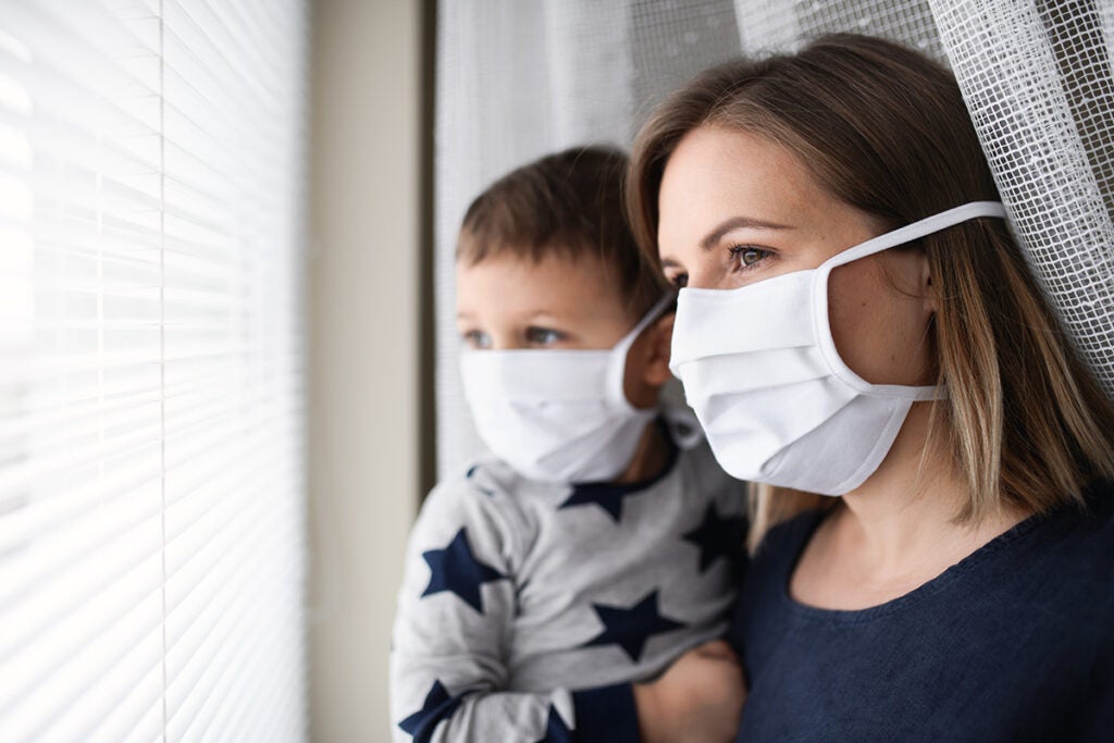 Mother and small son with face mask indoors at home, quarantine concept.