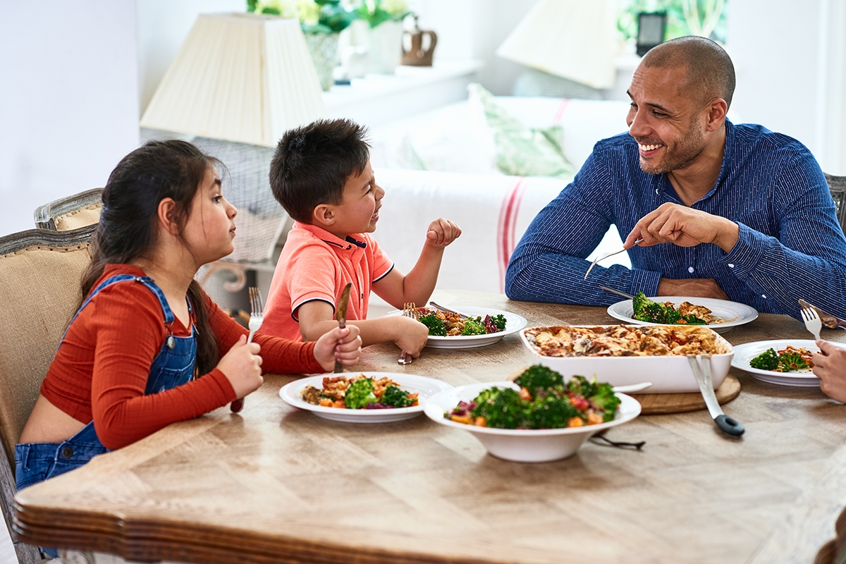 Cheerful father smiling and talking with family at meal time