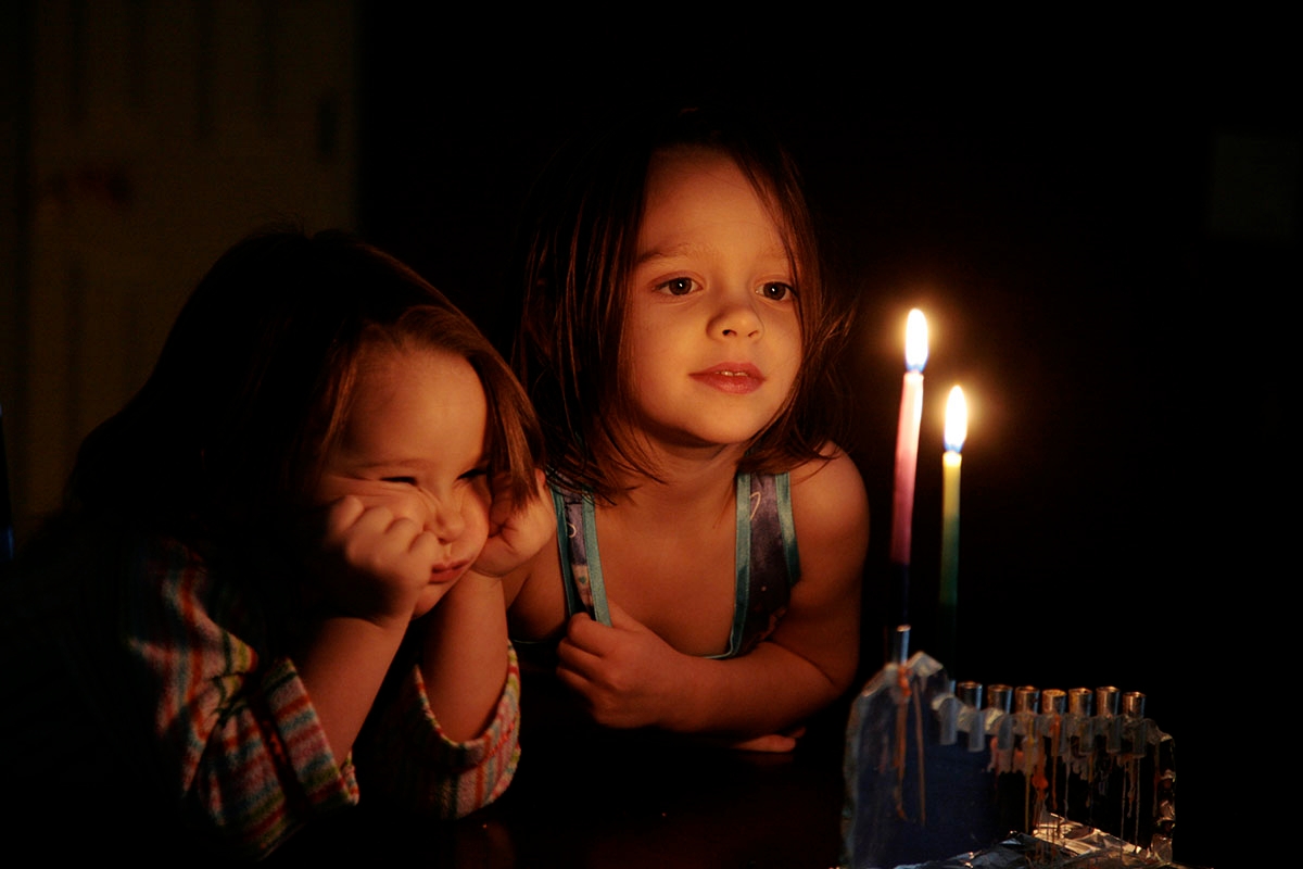 two young girls lighting a menorah