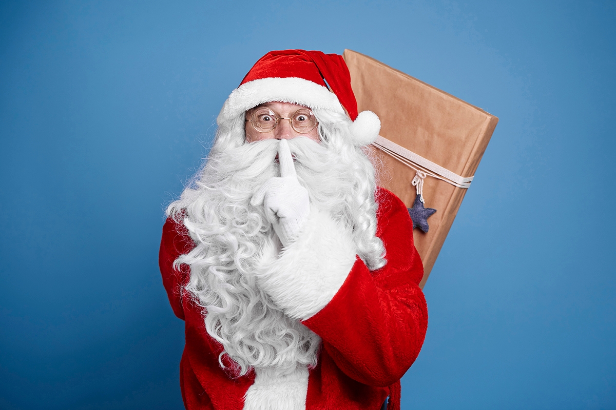Santa Claus holding christmas presents behind his back.