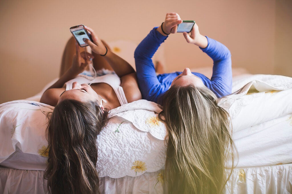 Teenage girls lying on bed looking at smart phones