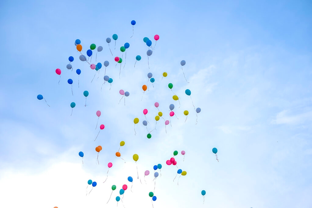 Colorful balloons flying away in blue sky.