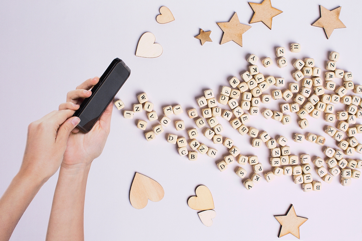 Hands holding a smartphone with letters, hearts and stars
