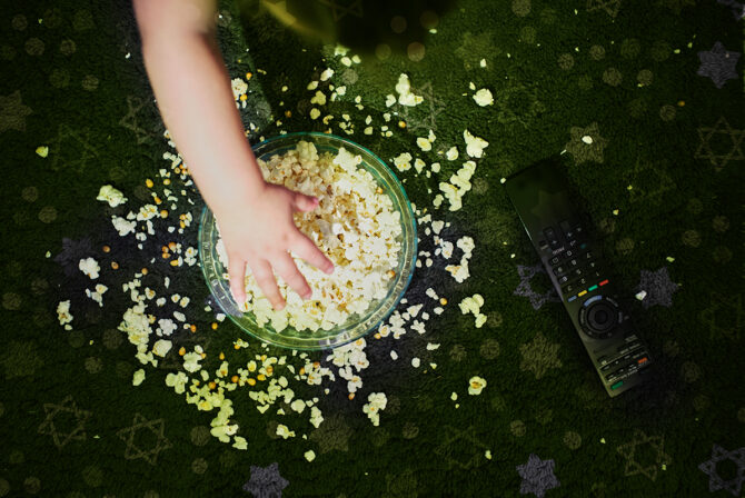a bowl of popcorn on the floor with a small child’s hand taking it fro
