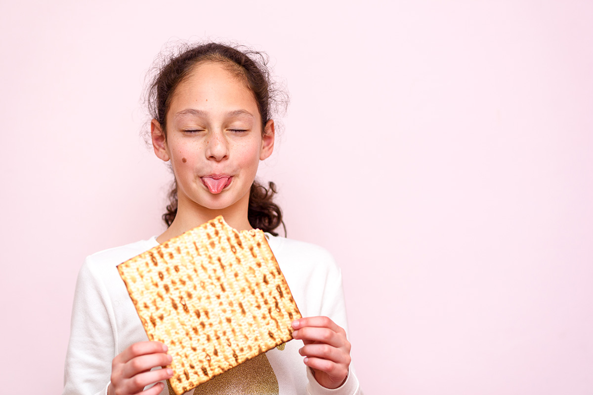 Portrait of the cute teenager girl holding matzah and shows tongue. Jewish child eating matzo unleavened bread in Jewish holidays Passover.