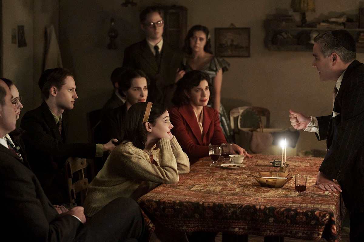 Jan and Miep Gies (Joe Cole and Bel Powley) join the Franks and the van Pels (from left: Liev Schreiber as Otto Frank, Ashley Brooke as Margot Frank, Rudi Goodman as Peter van Pels, Amira Casar as Edith Frank, Billie Boullet as Anne Frank and Caroline Catz as Mrs. van Pels) and watch as Mr. van Pels (Andy Nyman) lights the menorah during Hanukkah, as seen the upcoming limited series A SMALL LIGHT, from National Geographic and ABC Signature in partnership with Keshet Studios. (Photo credit: