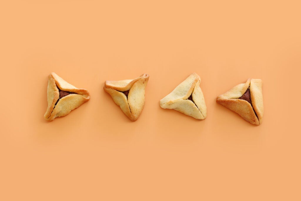 four hamantaschen in a row on an orange background