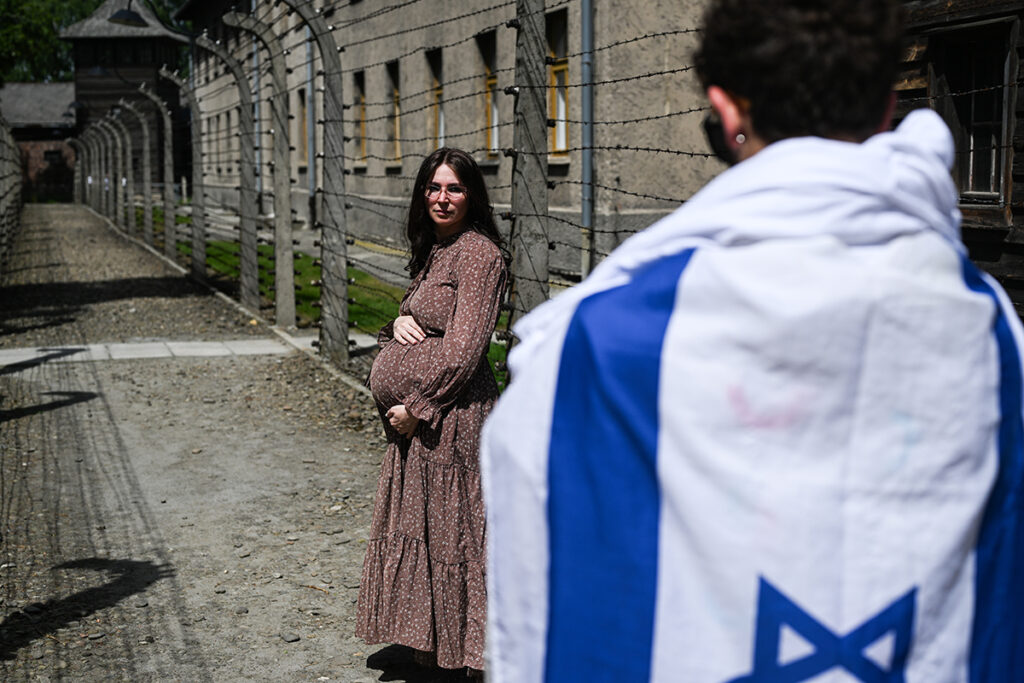 OSWIECIM, POLAND - MAY 06: A pregnant participant poses for a photo between a wired fence during the 36th March of the Living at the former Nazi concentration death camp Auschwitz I on May 06, 2024 in Oswiecim, Poland. The International March of the Living event takes place on Yom HaShoah, where thousands of people from around the world march the three kilometres between the prisoner of war camps, Auschwitz to Birkenau in memory of the holocaust victims of World War II.