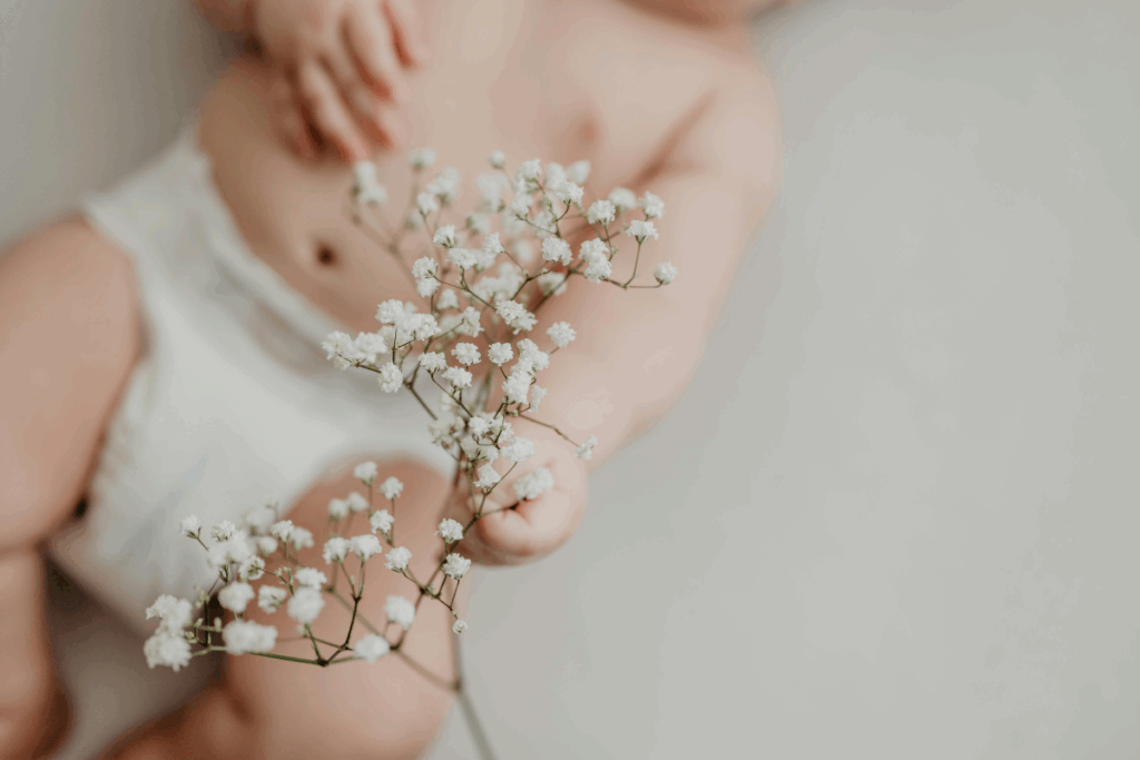 A photo of a baby grabbing at a small sprig of white flowers.