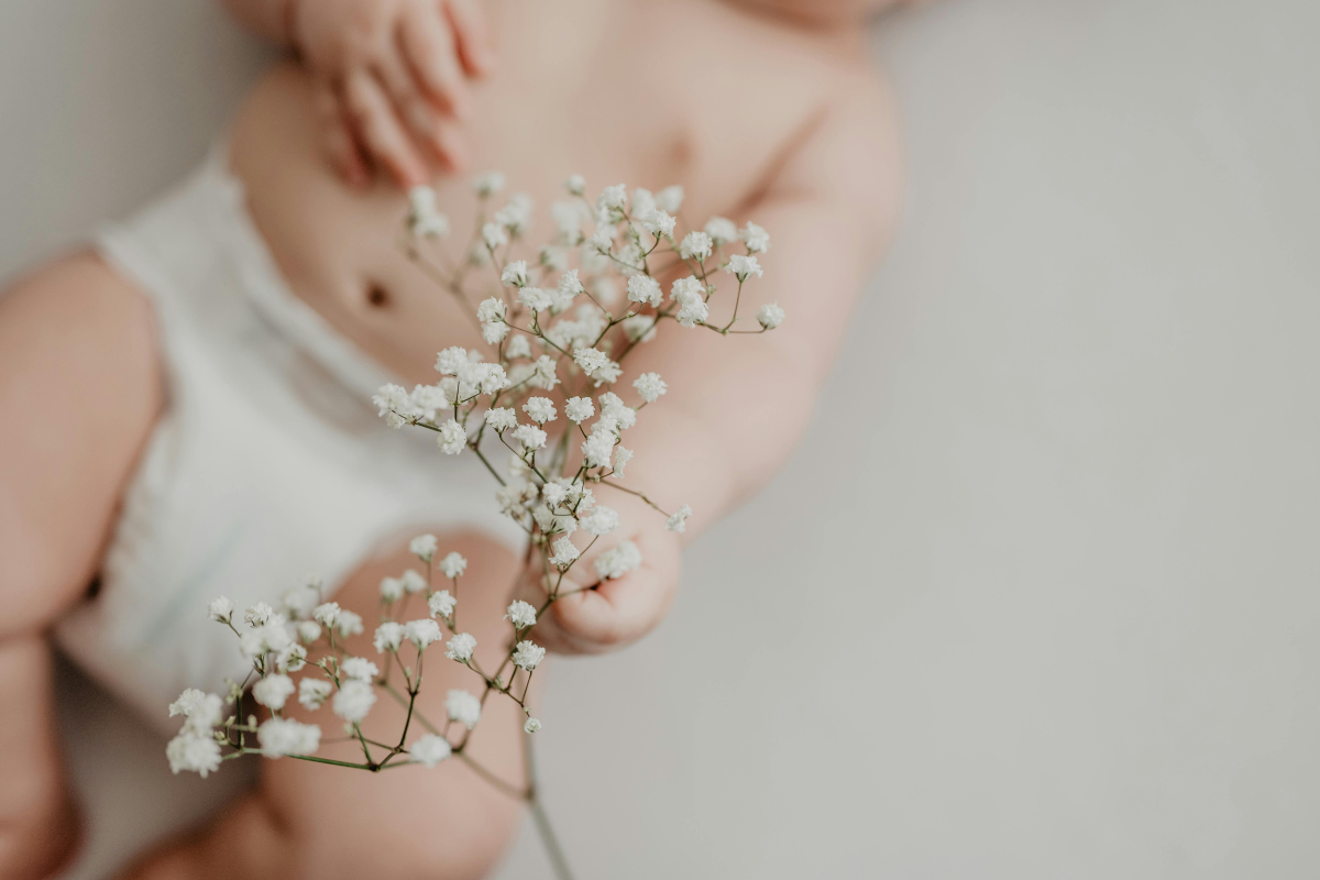 A photo of a baby grabbing at a small sprig of white flowers.
